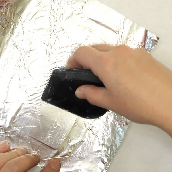 Smoothing aluminum foil on paper to be used in an art journal or card
