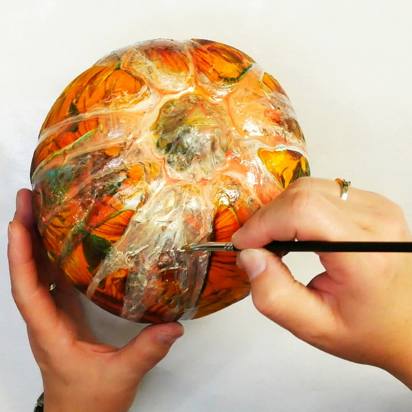Adding paint to a dried paint pour on a plastic pumpkin with napkin decoupage